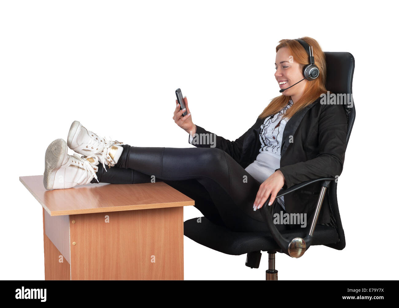 Giovane imprenditrice seduti rilassati in poltrona con lo smartphone, la cuffia e le gambe sulla scrivania. Isolato su bianco. Foto Stock