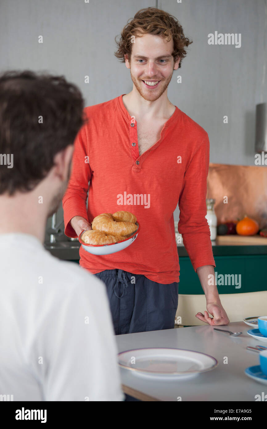Sorridente gay uomo con croissant nella piastra guardando il partner a casa Foto Stock