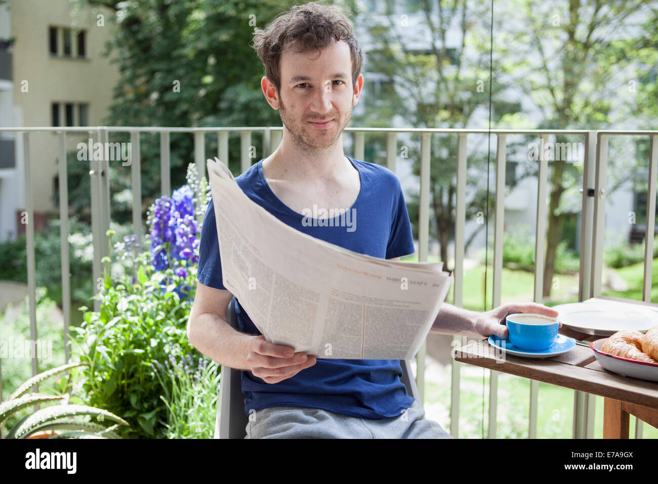 Ritratto di giovane uomo che legge il giornale mentre avente un caffè a portico Foto Stock