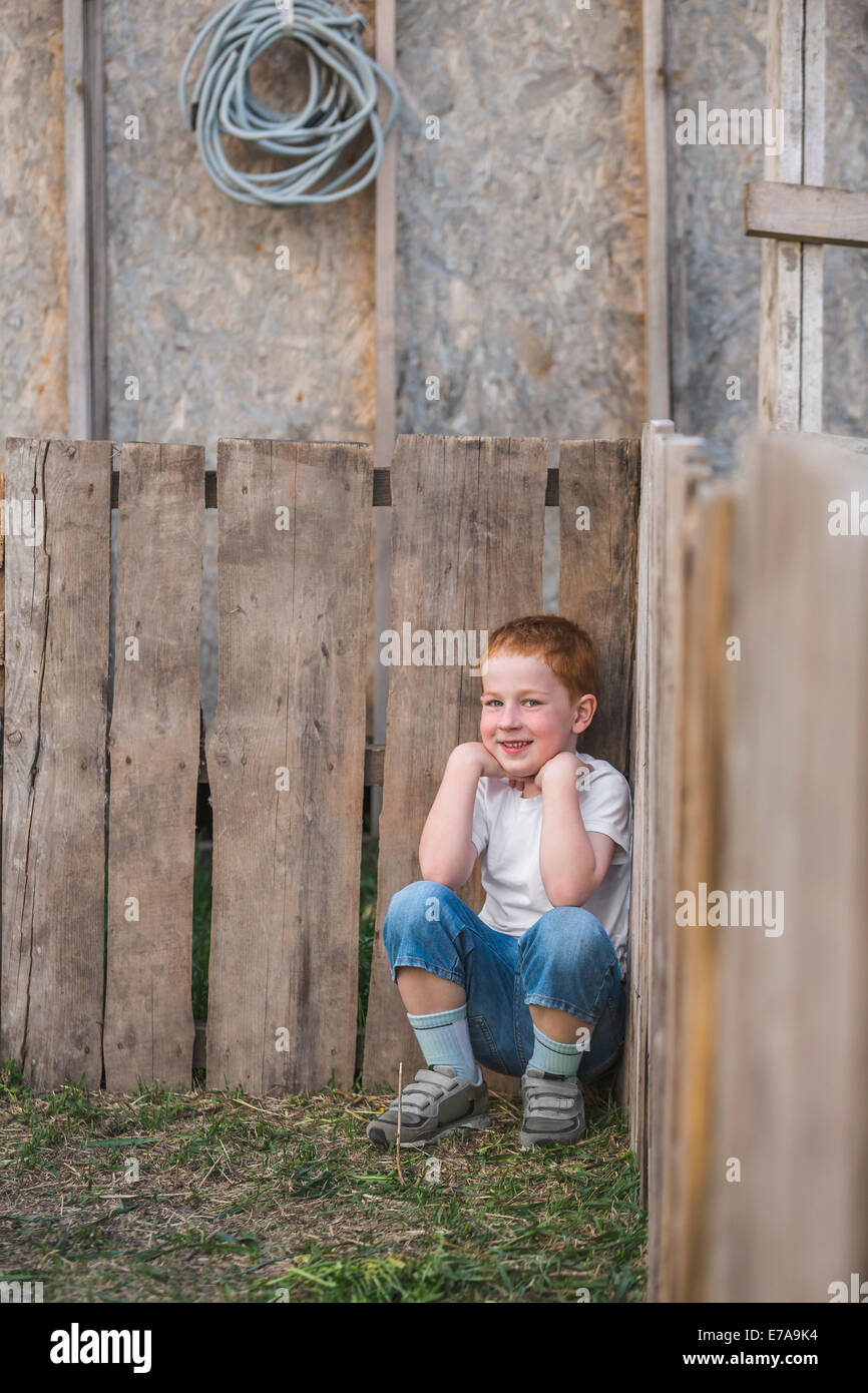 Ritratto di ragazzo accovacciato contro le tavole di legno in posizione di parcheggio Foto Stock