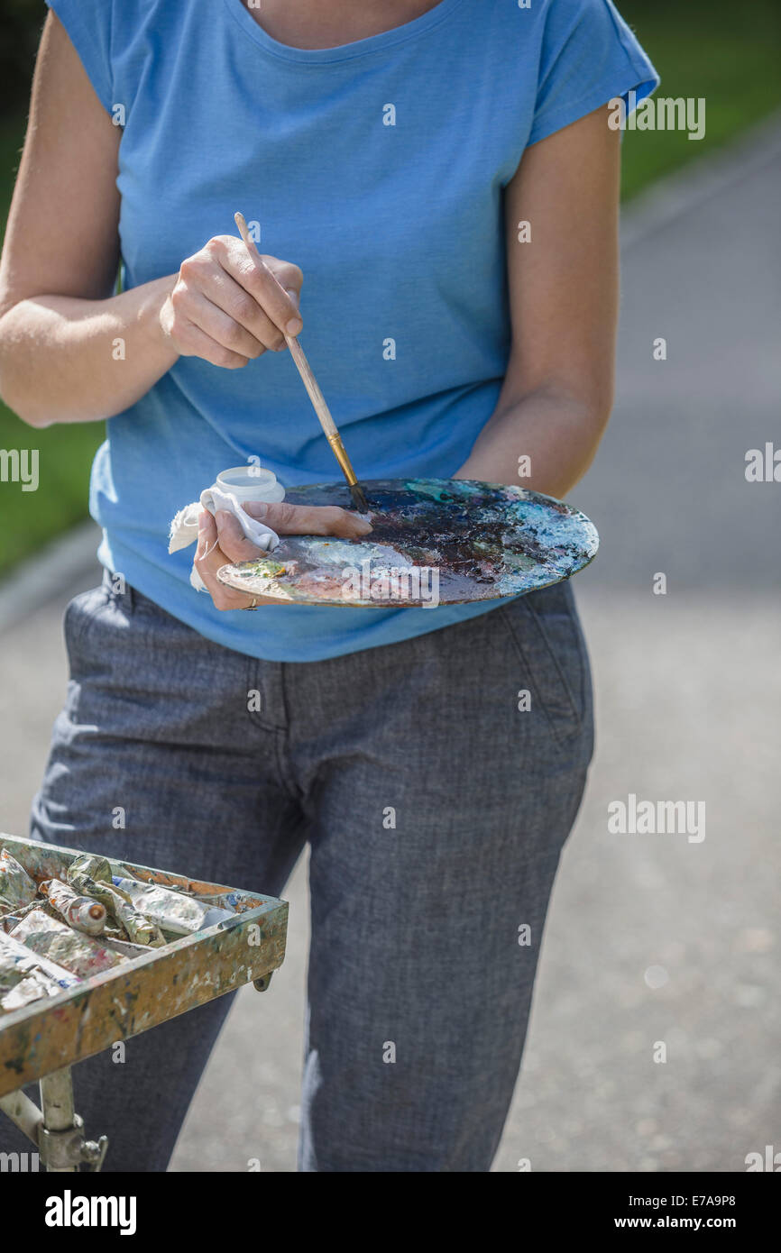 Sezione mediana del pittore femmina tenendo il pennello e la tavolozza dei colori in posizione di parcheggio Foto Stock