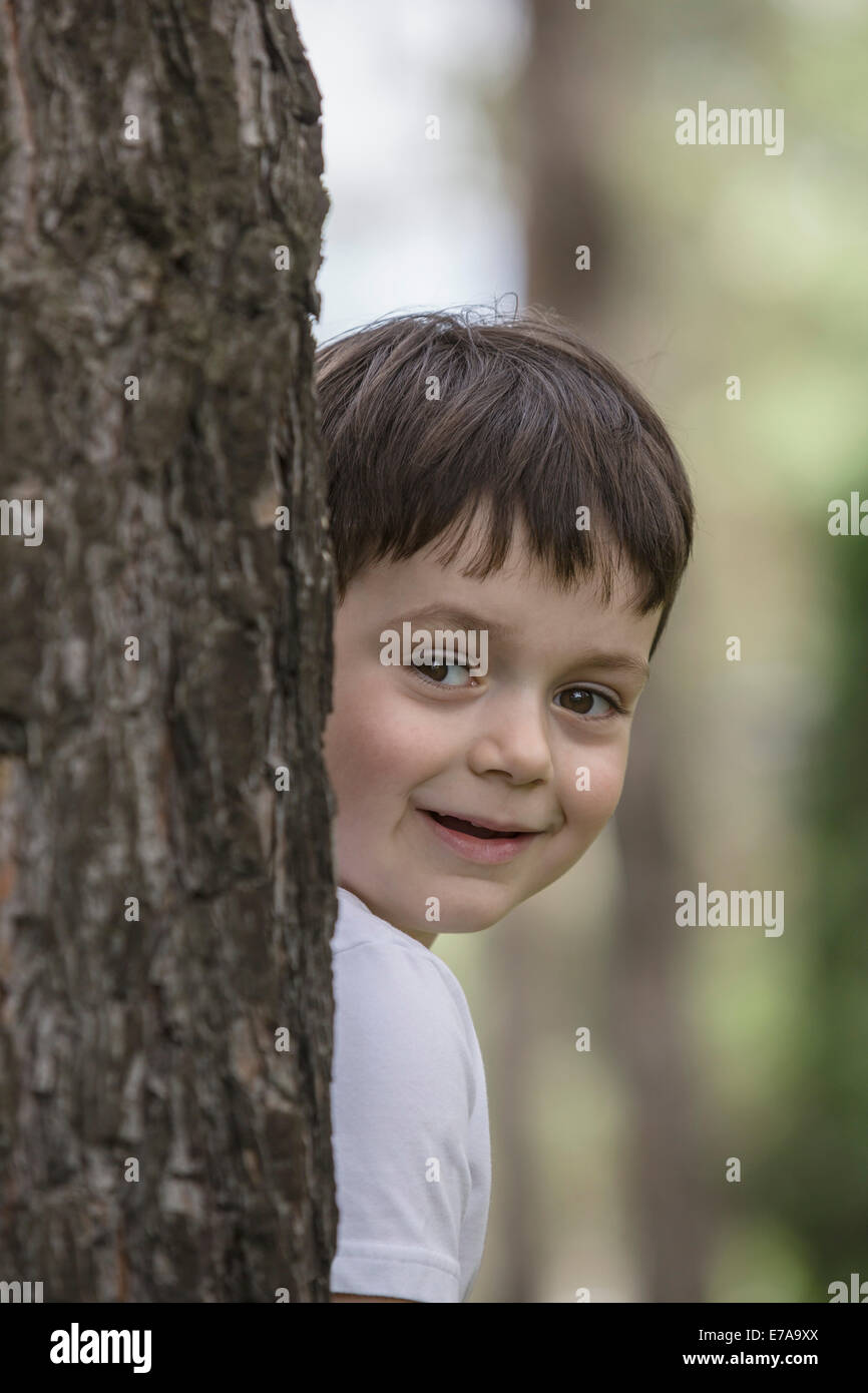Carino boy nascondersi dietro a tronco di albero in posizione di parcheggio Foto Stock