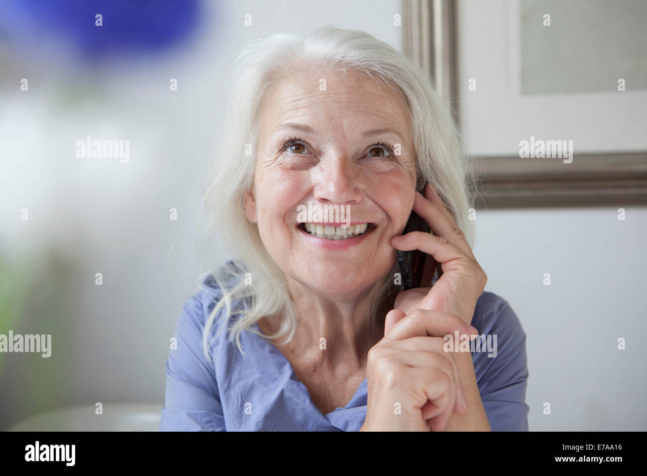 Felice senior donna che guarda verso l'alto mentre si risponde a telefono cellulare a casa Foto Stock