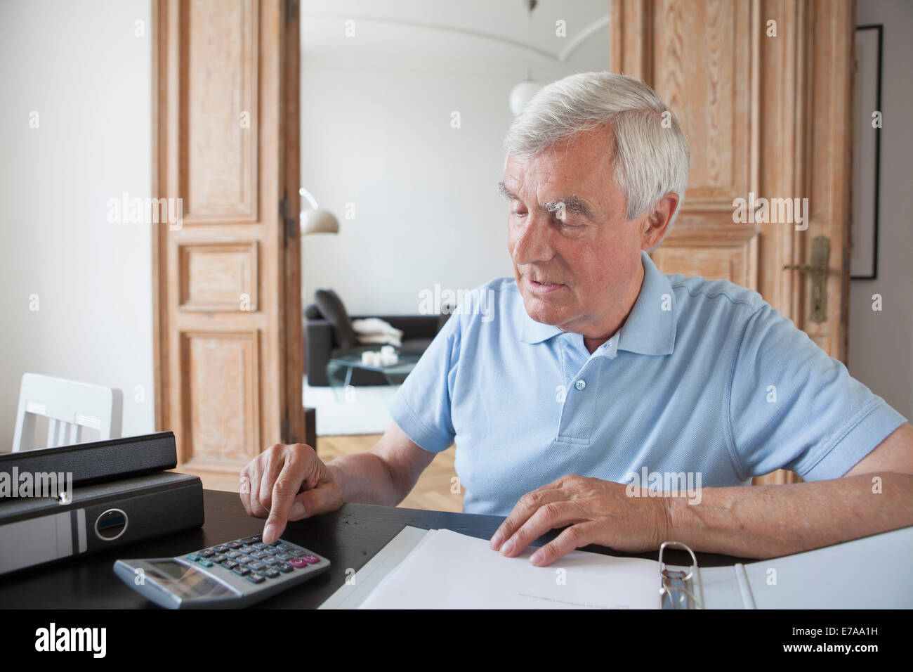 Senior uomo utilizzando la calcolatrice per calcolare home finanzia a tabella Foto Stock