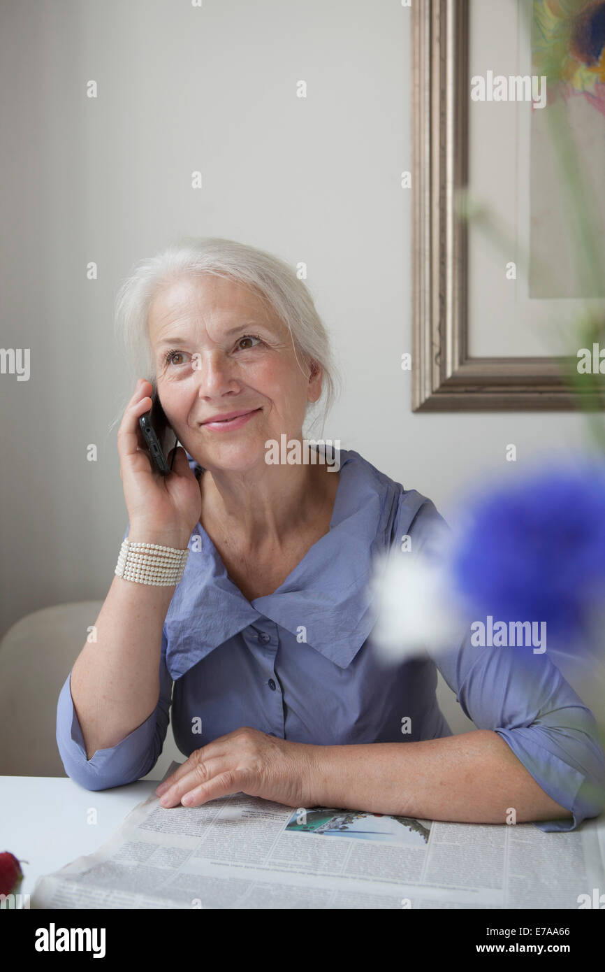Sorridente donna senior risposta cellulare a tavola Foto Stock