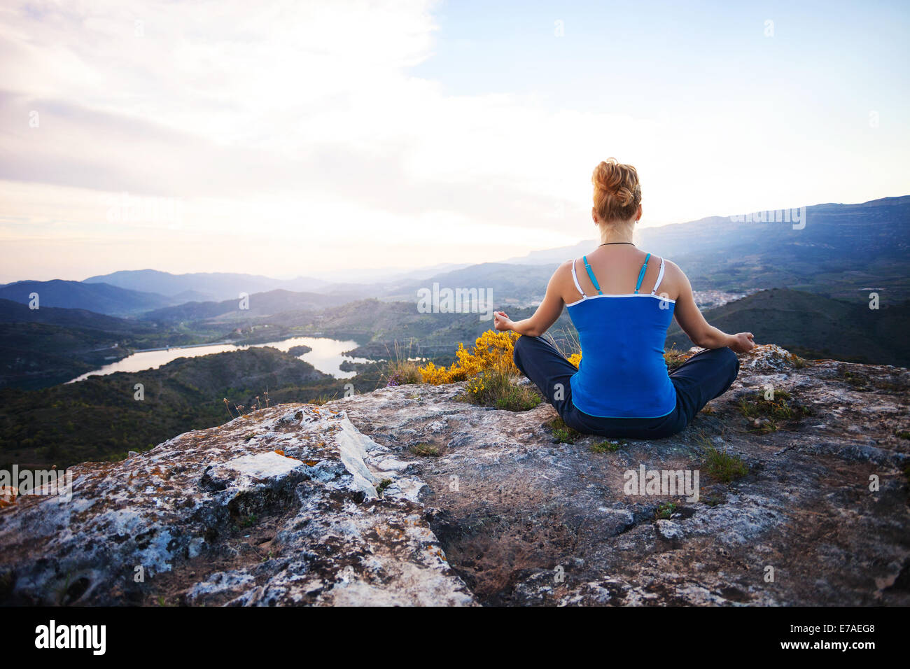 Giovane donna seduta su una roccia e godersi la vista della valle. La ragazza si siede nella posizione asana. Foto Stock