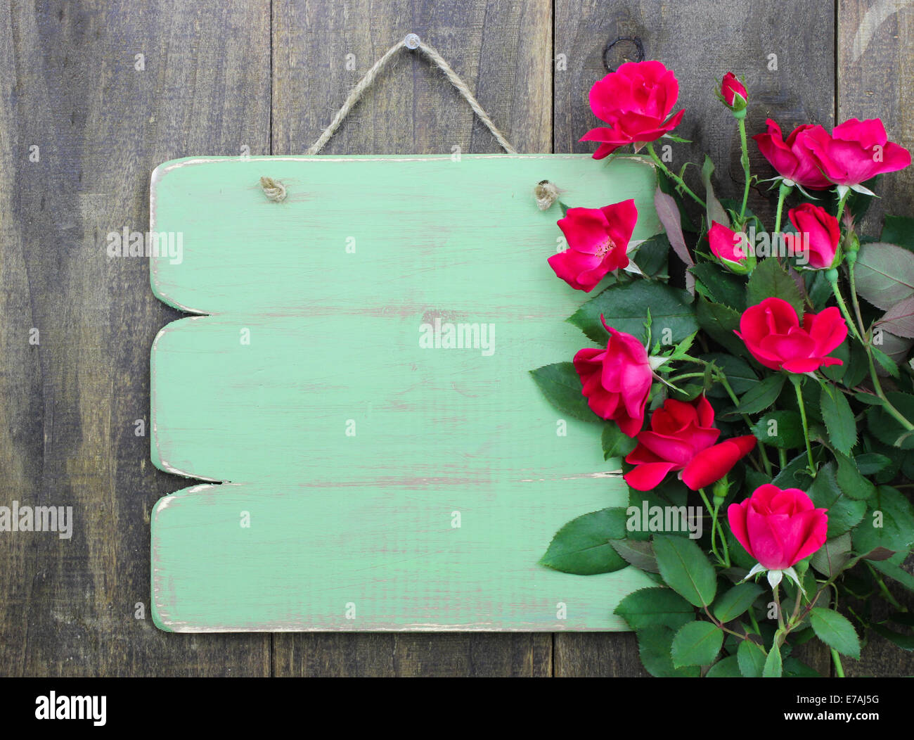Addolorato vuoto segno verde con bordo di fiori di rose rosse appese su legno rustico sfondo Foto Stock