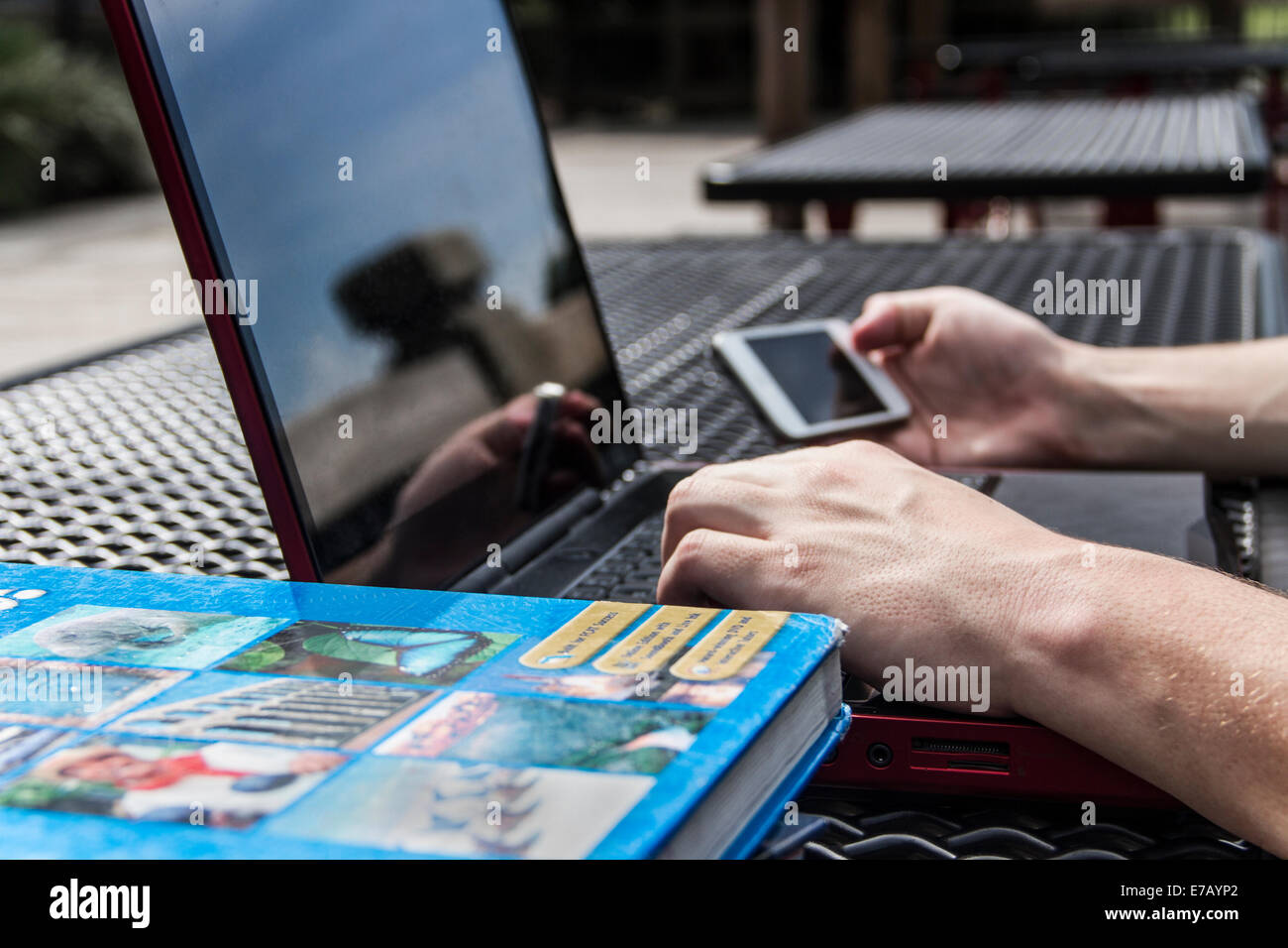 Uomo con il cellulare mentre sul computer portatile con un libro di testo nelle vicinanze. Foto Stock
