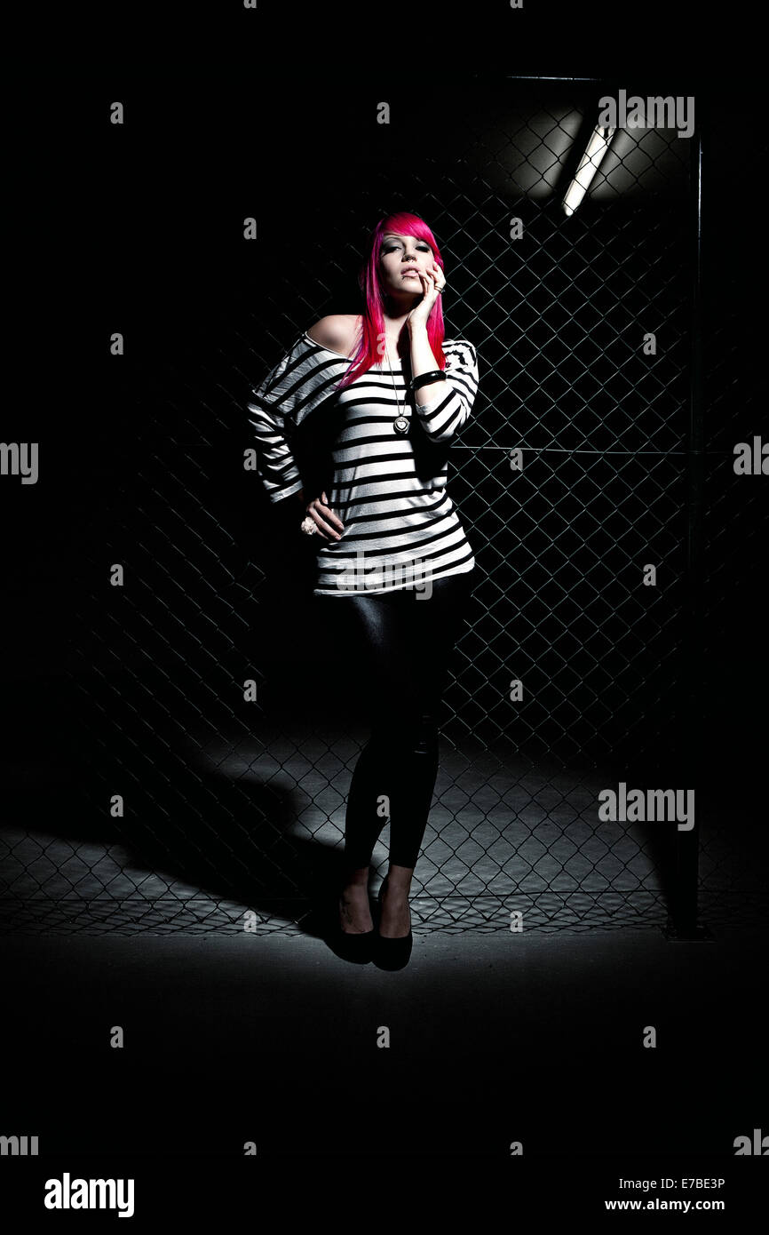 Donna con capelli rosa di fronte a una catena di recinzione di collegamento Foto Stock