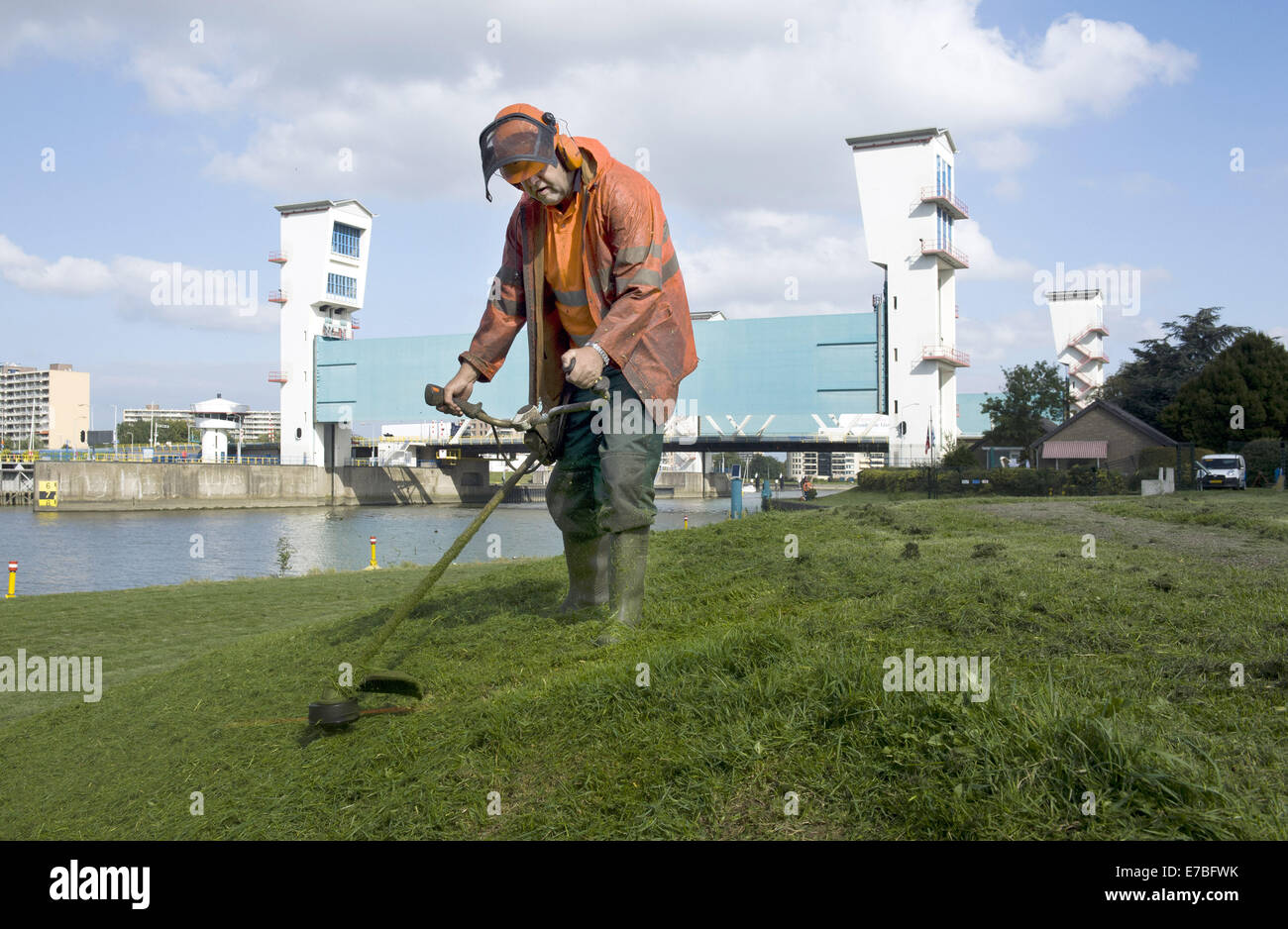 Sett. 10, 2014 - Rotterdam South Holland, Paesi Bassi Olanda - un uomo è Falciare il prato da una diga e nella parte anteriore del Dutch Ijssel dam. Il Hollandse IJssel (Olandese IJssel) collega Rotterdam con il Mare del Nord. In caso di alluvione, il fiume di acqua potrebbe non essere in grado di scorrere lontano perché la risalita di acqua di mare ad arrestarlo. Il fiume avrebbe pertanto burst facilmente le sue rive. Vi sono due motivi principali per la ricerca di una soluzione per il pericolo di inondazione: in primo luogo, il Hollandse Issel fluisce attraverso il più basso giacente zona dei Paesi Bassi. In secondo luogo, questa è una delle aree più densamente popolate del N Foto Stock