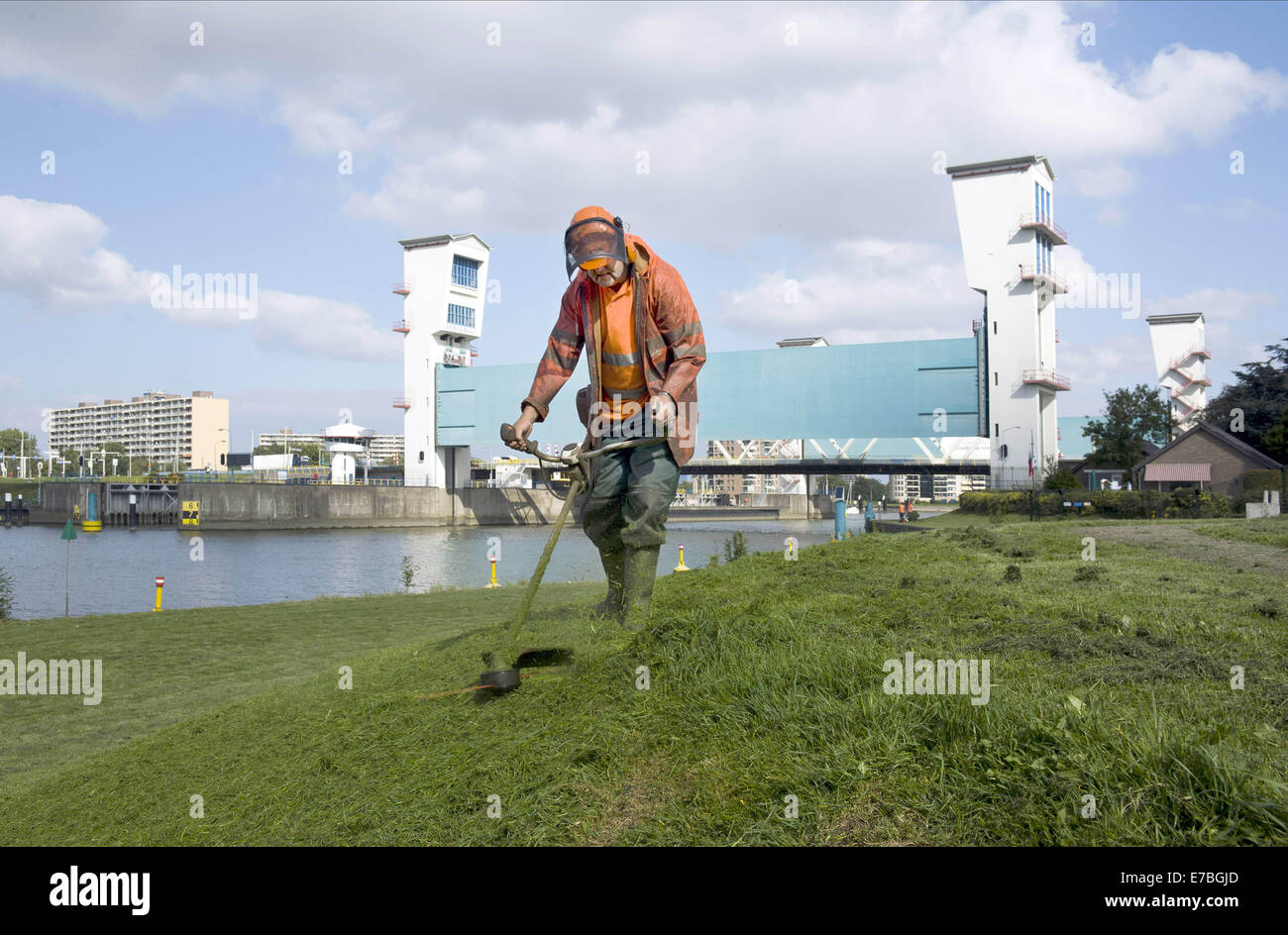 Sett. 10, 2014 - Un uomo è Falciare il prato da una diga e nella parte anteriore del Dutch Ijssel dam. Il Hollandse IJssel (Olandese IJssel) collega Rotterdam con il Mare del Nord. In caso di alluvione, il fiume di acqua potrebbe non essere in grado di scorrere lontano perché la risalita di acqua di mare ad arrestarlo. Il fiume avrebbe pertanto burst facilmente le sue rive. Vi sono due motivi principali per la ricerca di una soluzione per il pericolo di inondazione: in primo luogo, il Hollandse Issel fluisce attraverso il più basso giacente zona dei Paesi Bassi. In secondo luogo, questa è una delle aree più densamente popolate del Paesi Bassi. Inizialmente, la costruzione di un semi-chiuso mi dam Foto Stock