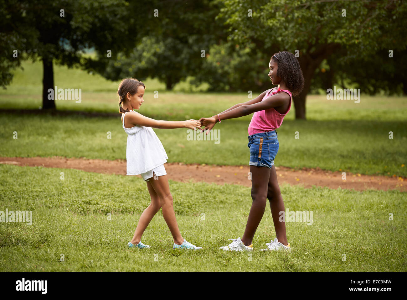 Due ispanici e africana di bambine la riproduzione ad anello attorno al rosie nel parco pubblico e tenendo le mani Foto Stock