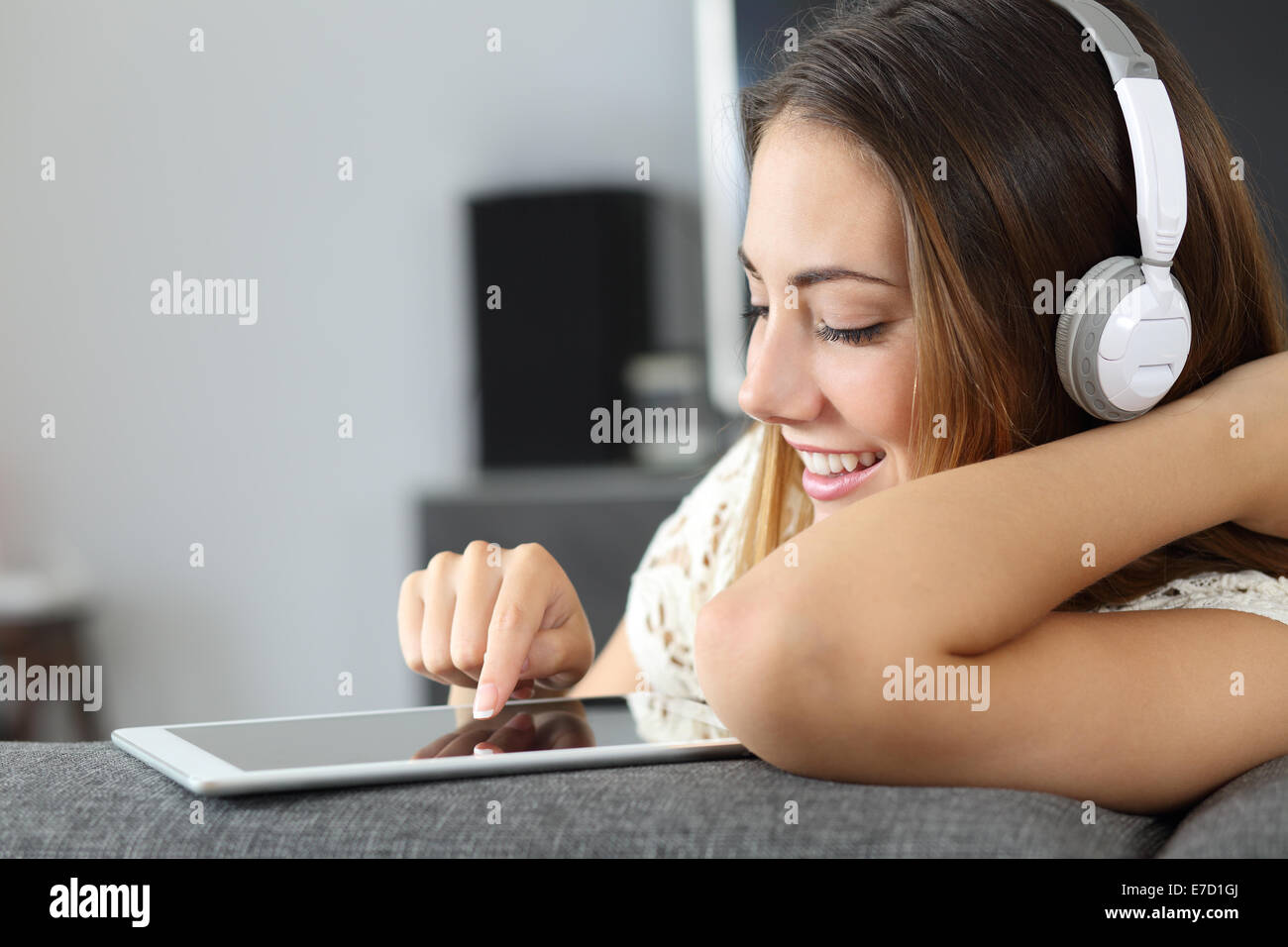 Donna felice ascoltando la musica da una pastiglia seduto su un divano a casa Foto Stock