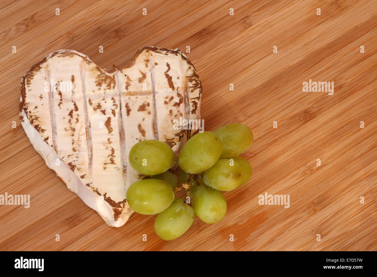 Formaggio Neufchatel conformata come cuore con uve sul tagliere di legno Foto Stock