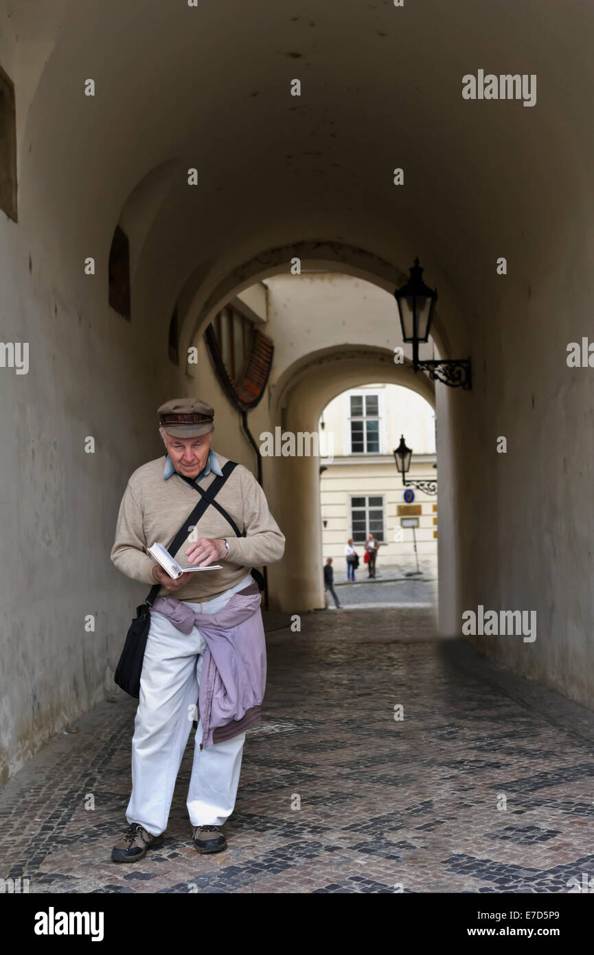 Un maschio senior leggendo un libro in un vicolo nella città di Praga, Repubblica Ceca. Foto Stock