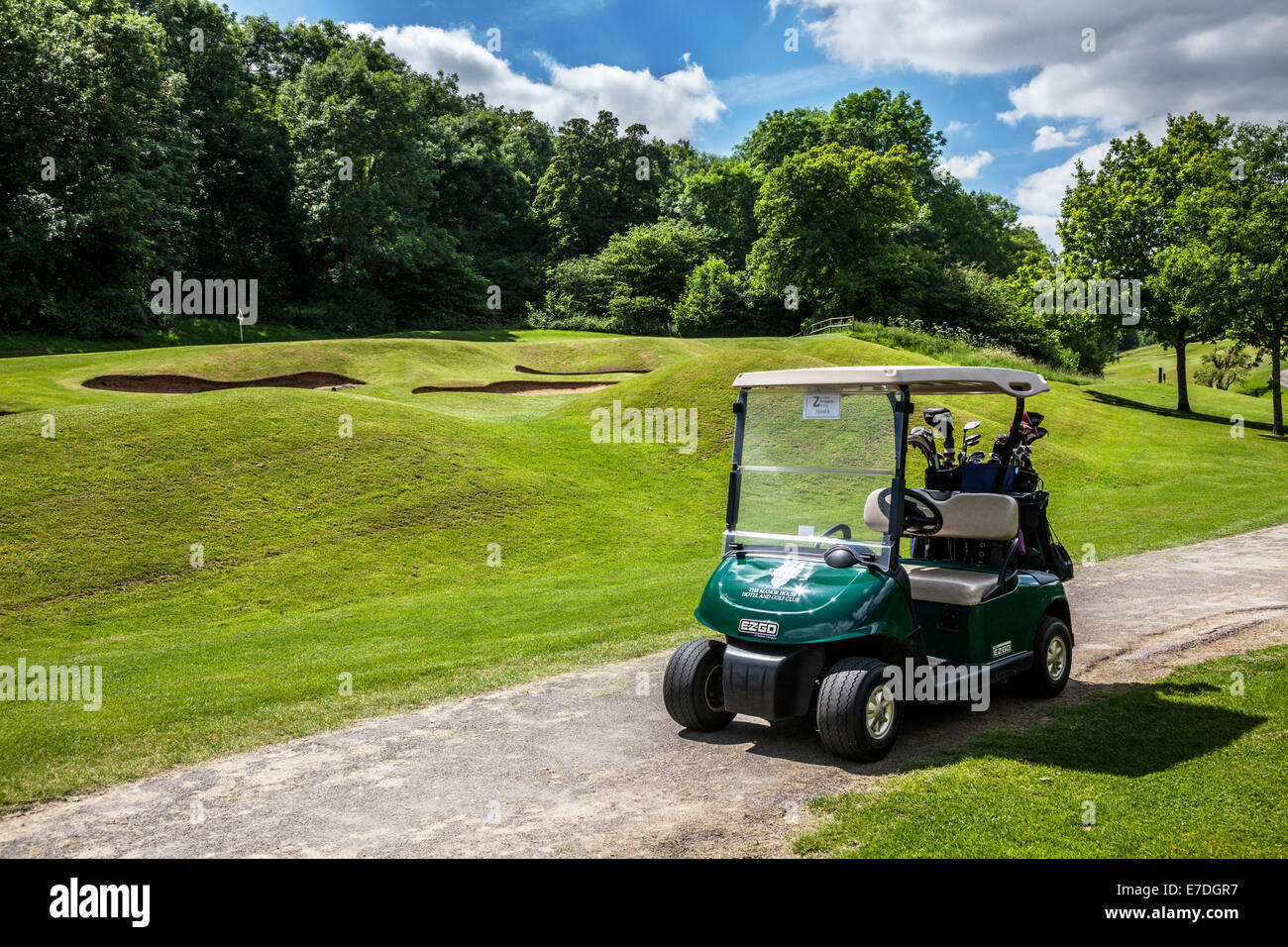 Bunker da un putting green con flagstick e foro e un buggy elettrico o il carrello su un tipico campo da golf. Foto Stock