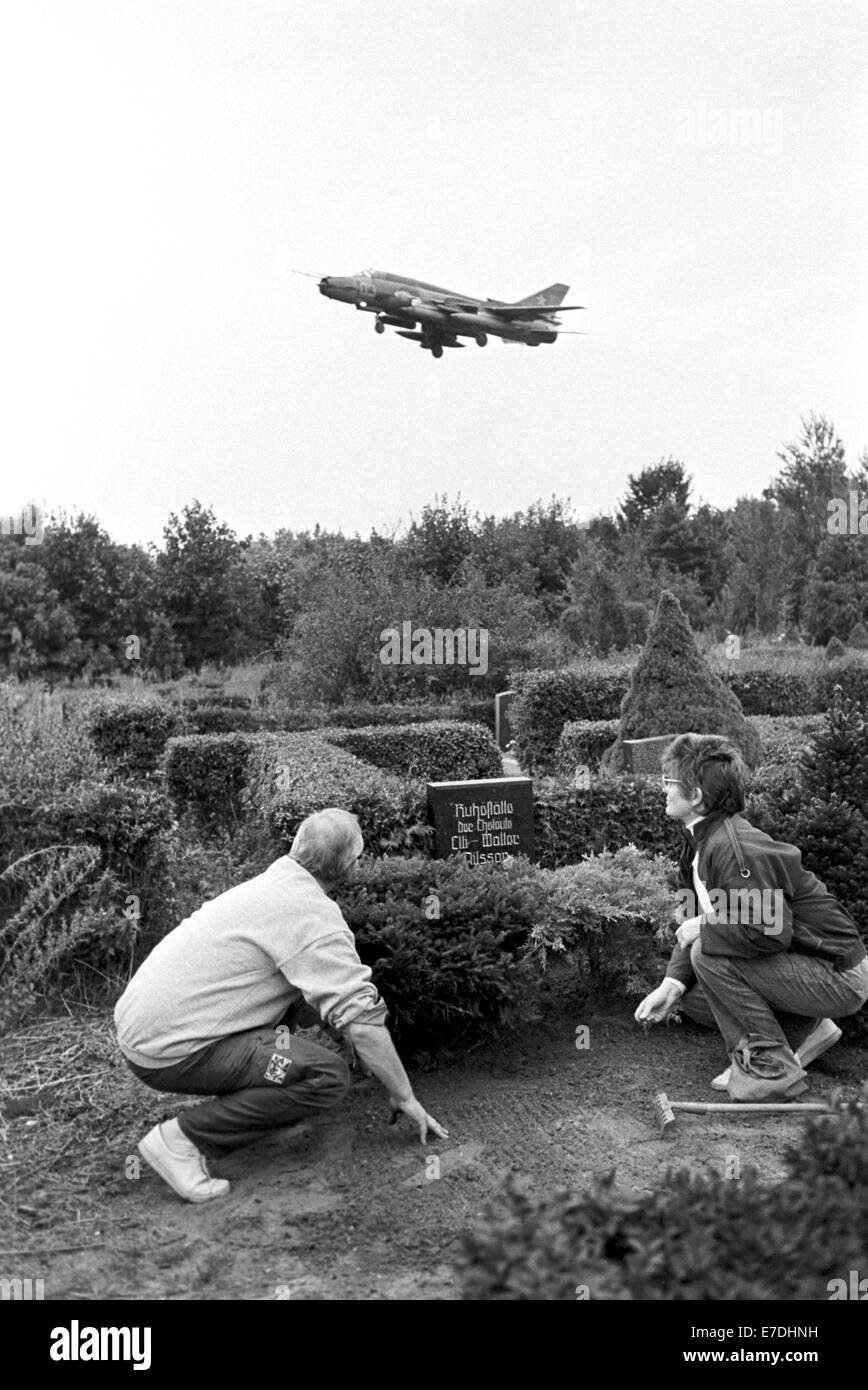 Una donna e un uomo tendono una tomba in un cimitero e anatra sul terreno come un jet da combattimento si avvicina a terra presso l'aerodromo militare 200 metri dietro il cimitero nel settembre 1990. Foto: Ernst-Ludwig Bach Foto Stock