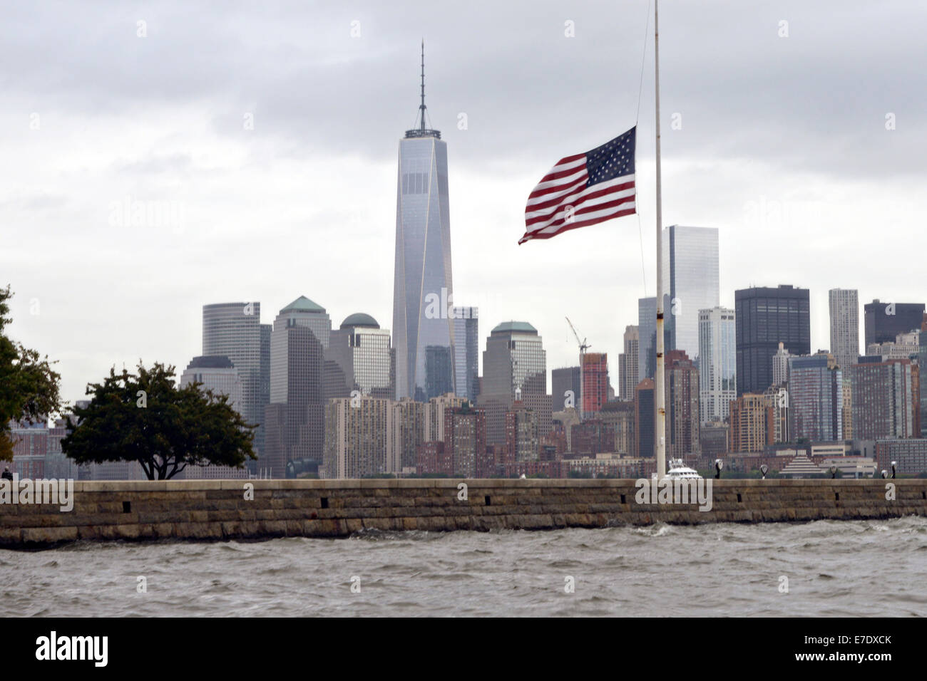La bandiera americana su Ellis Island a metà del personale in un giorno nuvoloso con la Freedom Tower e lo skyline di Manhattan durante il tredicesimo anniversario del 9/11 gli attentati terroristici di settembre 11, 2014. Foto Stock