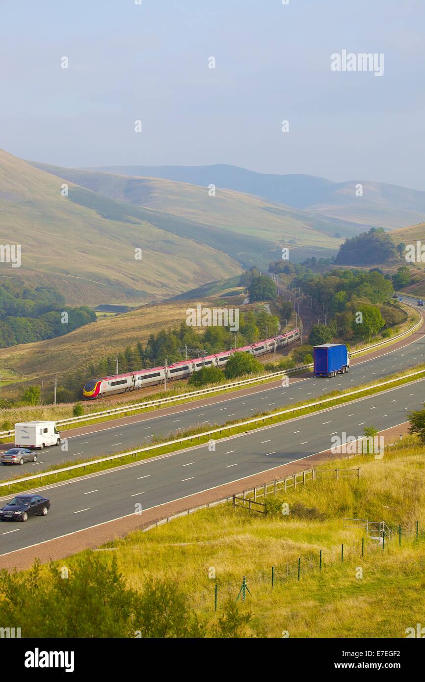 Classe 390 Pendolino Virgin treno passa l autostrada M6 nel fiume Lune Valley. Howgills, Cumbria, Linea principale della costa occidentale, UK. Foto Stock