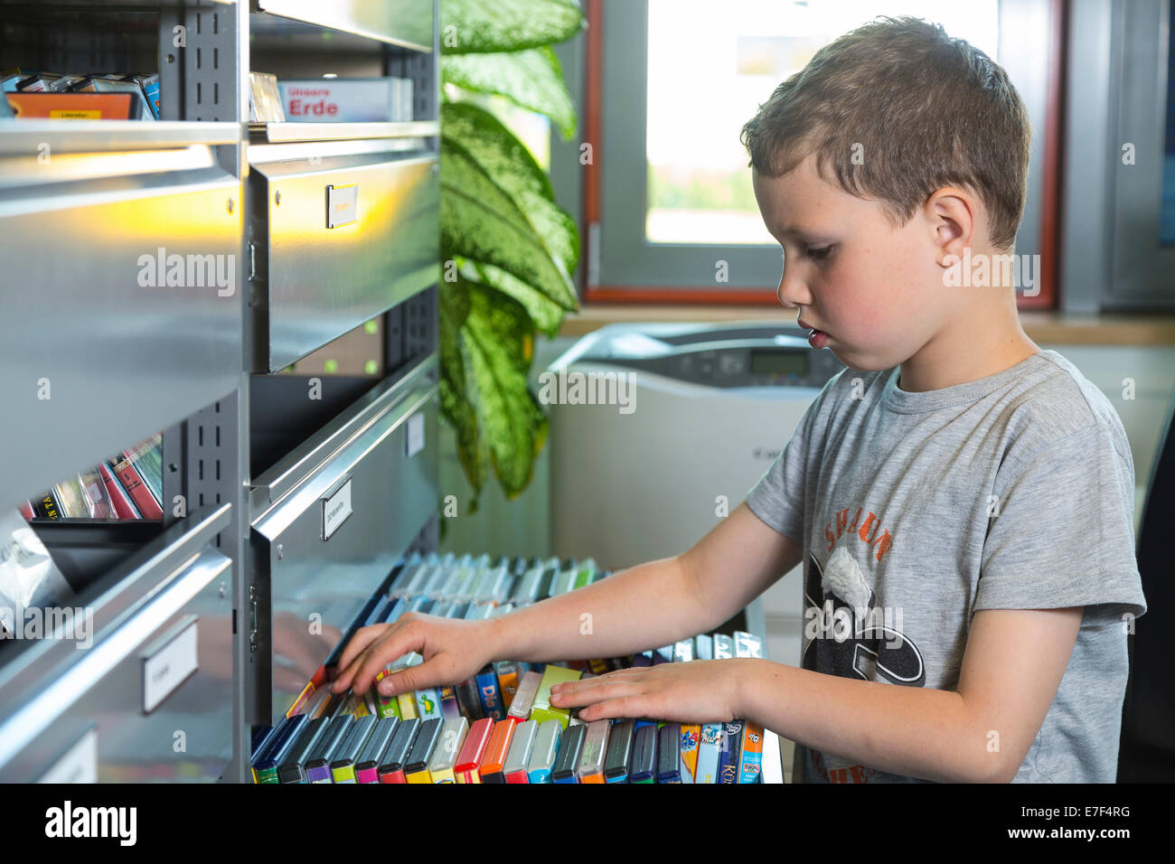 Il ragazzo, 7 anni, guardando per pellicole dei bambini al ripiano di DVD, media library della biblioteca della città, Coswig, Bassa Sassonia, Germania Foto Stock