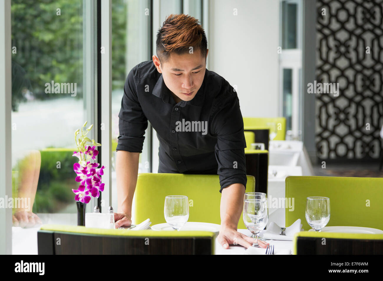 Cameriere asiatico nella tabella di impostazione in ristorante Foto Stock