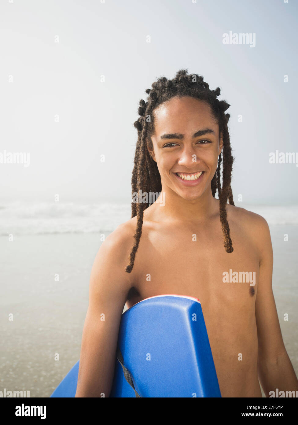 Nero ragazzo adolescente che trasportano boogie board sulla spiaggia Foto Stock