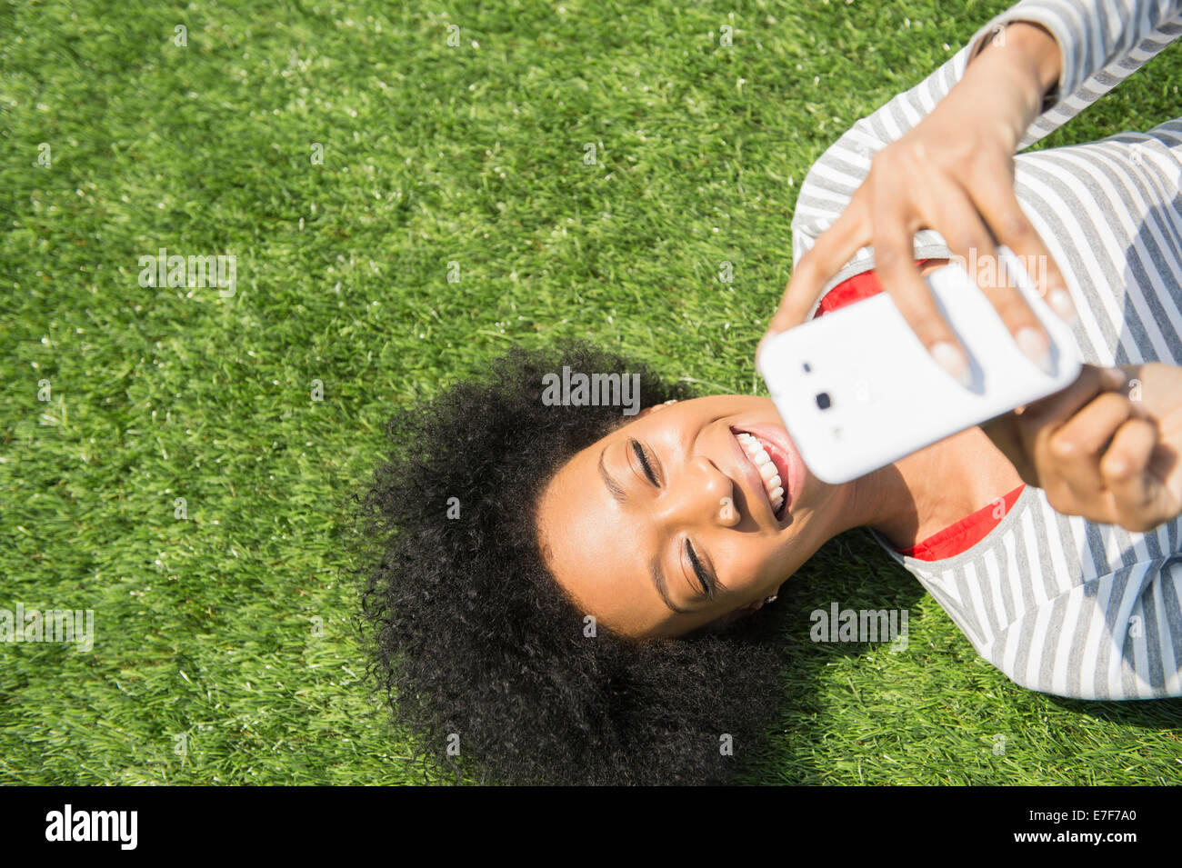 African American donna posa in erba tramite telefono cellulare Foto Stock