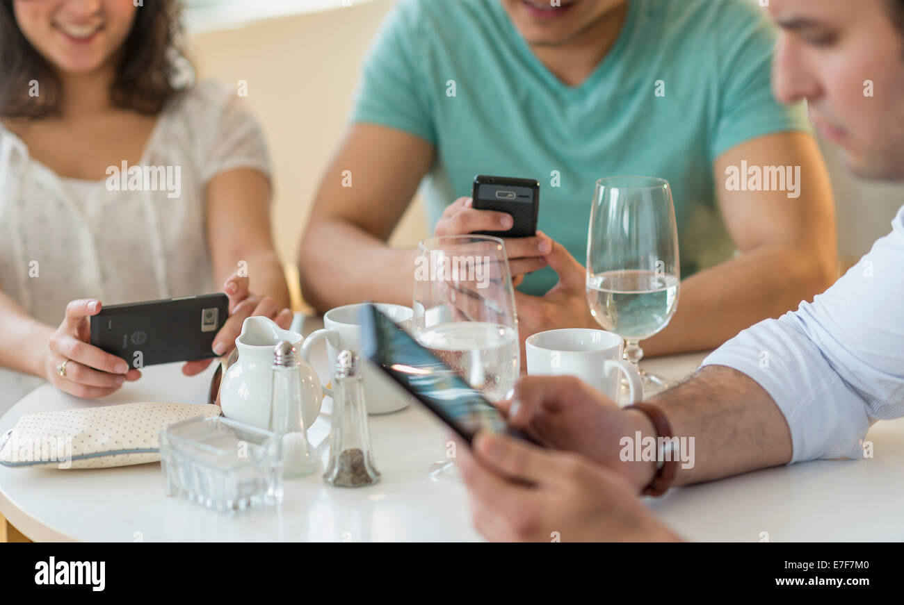 Amici ispanica utilizzando i telefoni cellulari in cafe Foto Stock