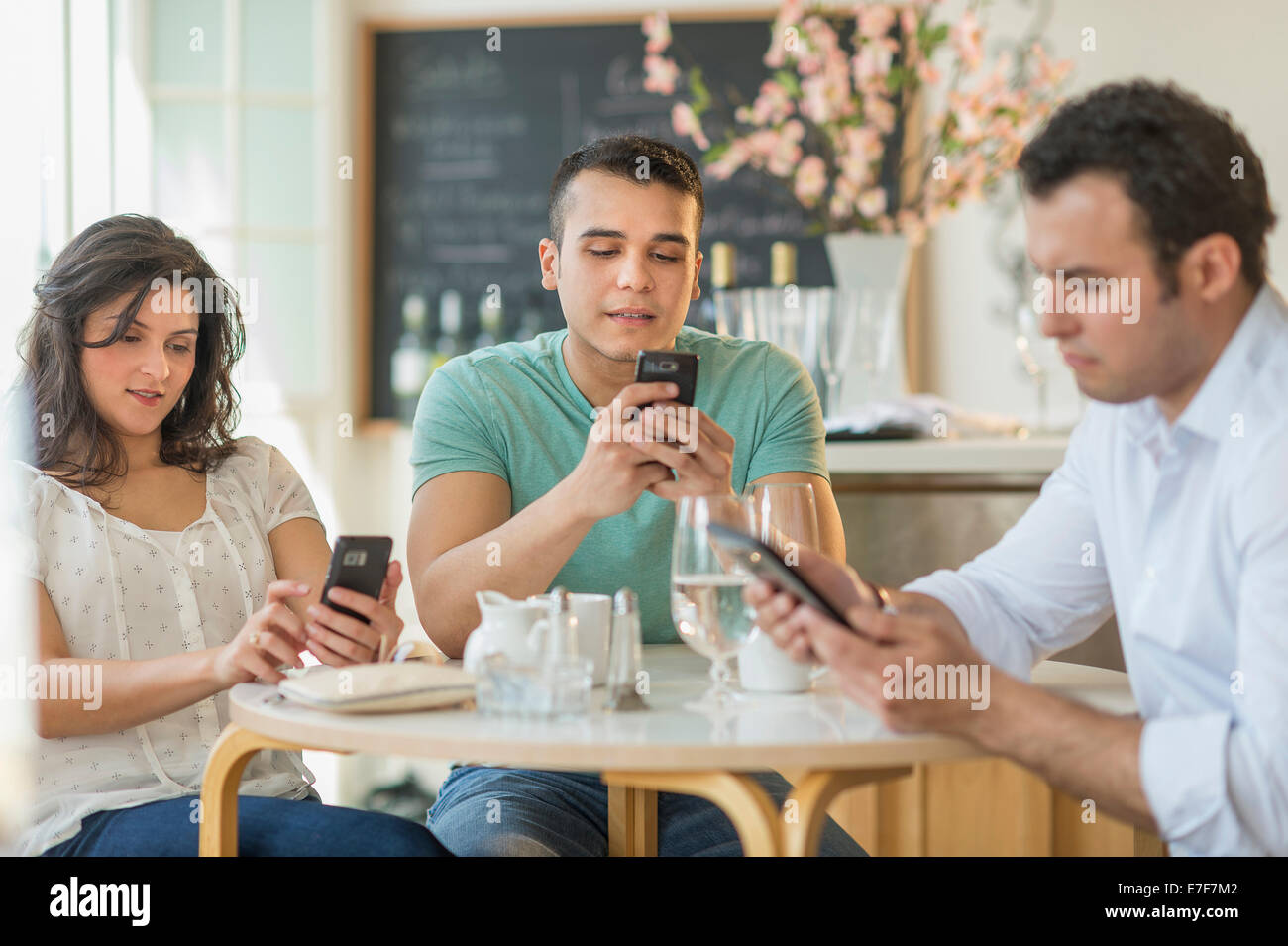Amici ispanica utilizzando i telefoni cellulari in cafe Foto Stock