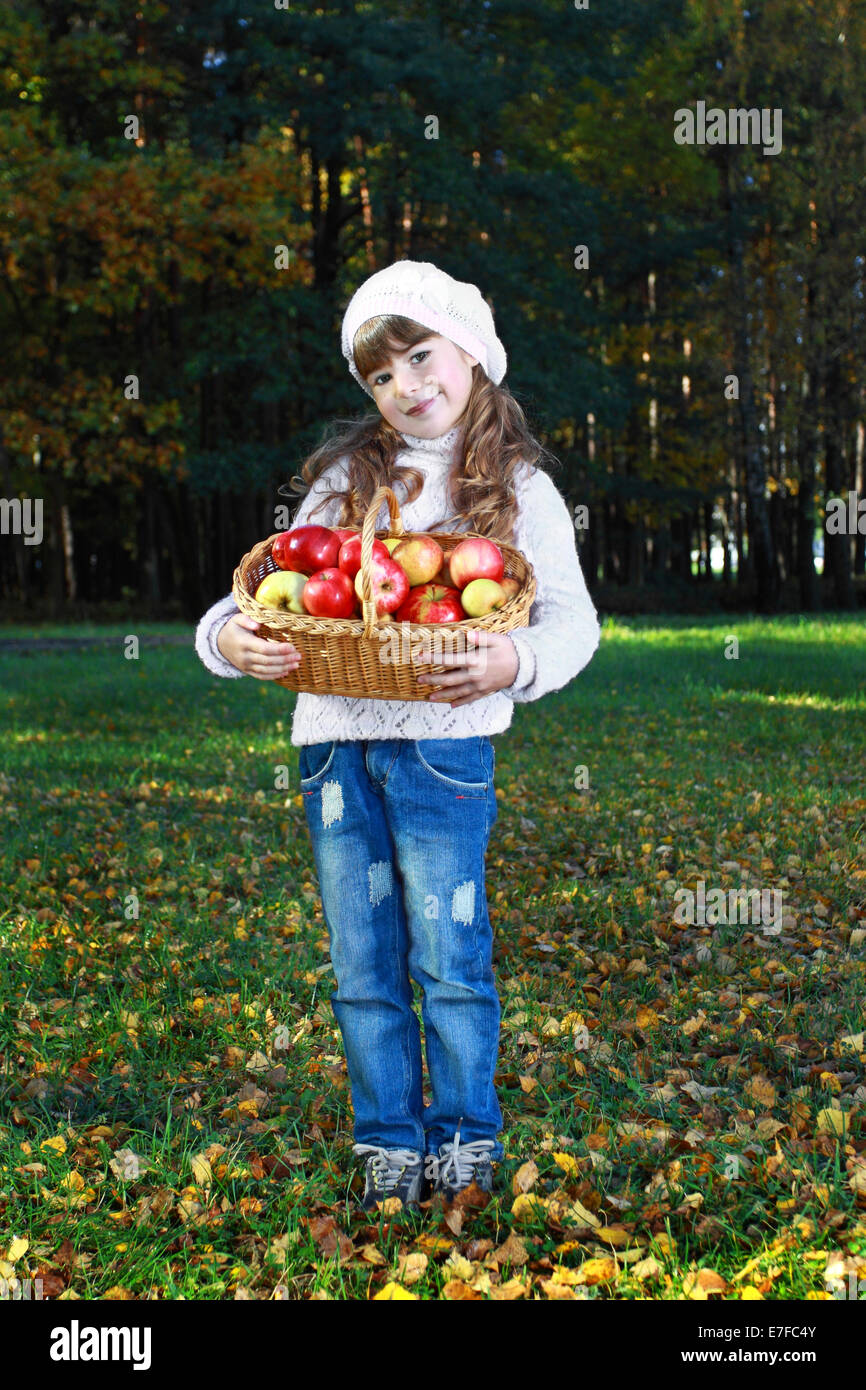 Carina ragazza con cesto di mele in mani. Ritratto all'aperto sul naturale sfondo di autunno Foto Stock