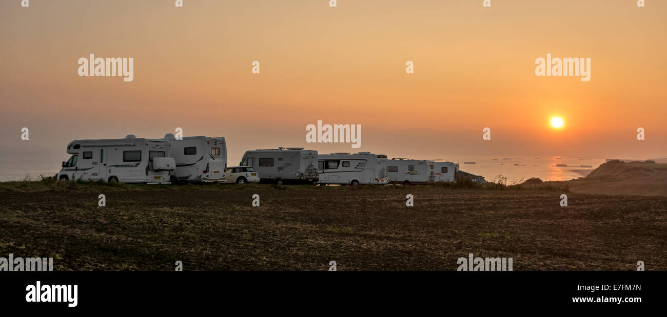 Fila di camper parcheggiato in un parcheggio per roulotte / veicolo per attività ricreative lungo la costa al tramonto con vista sul mare Foto Stock
