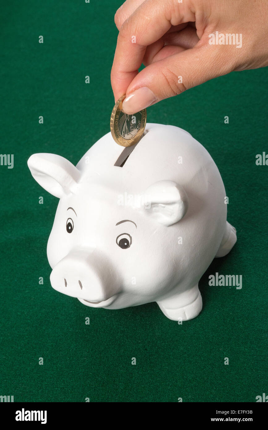 Salvadanaio di risparmio di denaro a due British pound coin andando nello slot Foto Stock