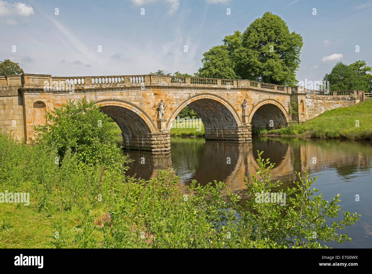 Ornato del XVIII secolo in pietra arenaria tre archi ponte sul fiume Derwent, con ponte alberi e cielo blu riflessa in acqua calma Foto Stock