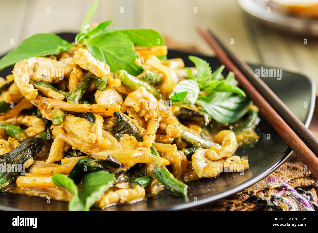 Pollo saltati in padella con cipolla, aglio, pasta di curry, long bean, germogli di bambù e latte di cocco, servita con basilico tailandese Foto Stock