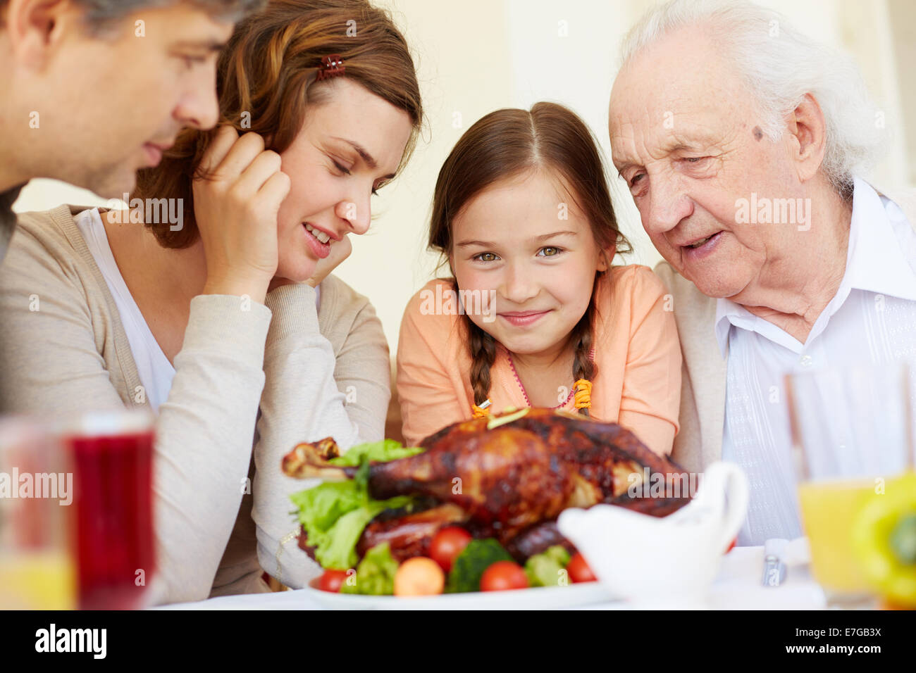 Ritratto di famiglia felice seduti a tavola festiva e guardando in avanti per mangiare gustoso tacchino Foto Stock