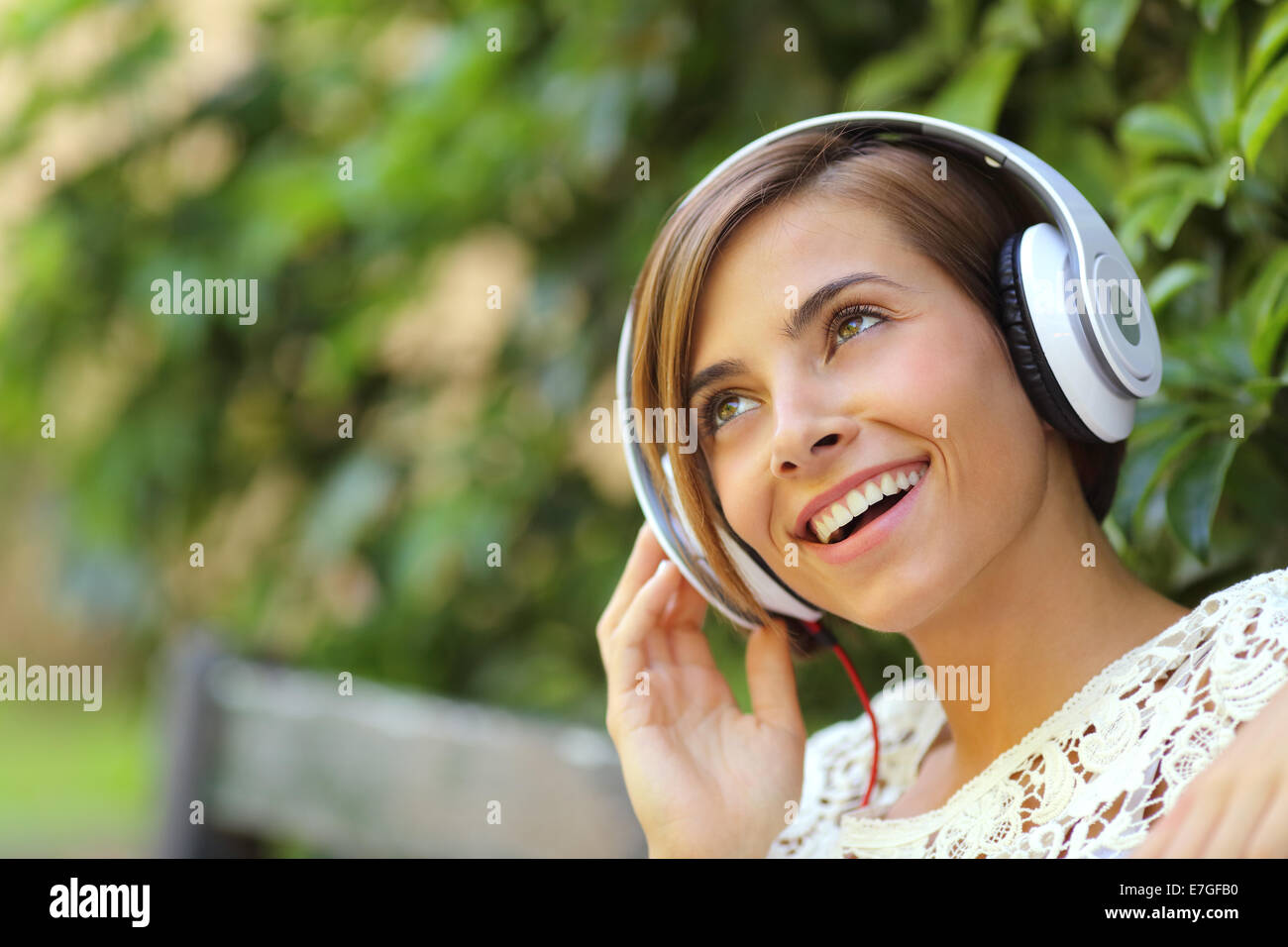 Ragazza ascoltando la musica con le cuffie in un parco con una verde sfondo sfocato Foto Stock