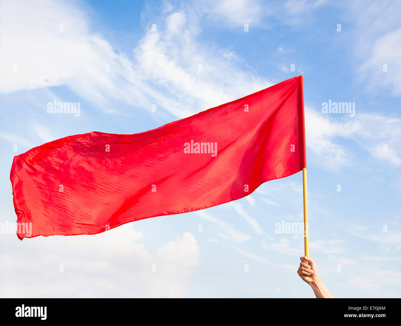 Mano sventola una bandiera rossa con cielo blu sullo sfondo Foto Stock