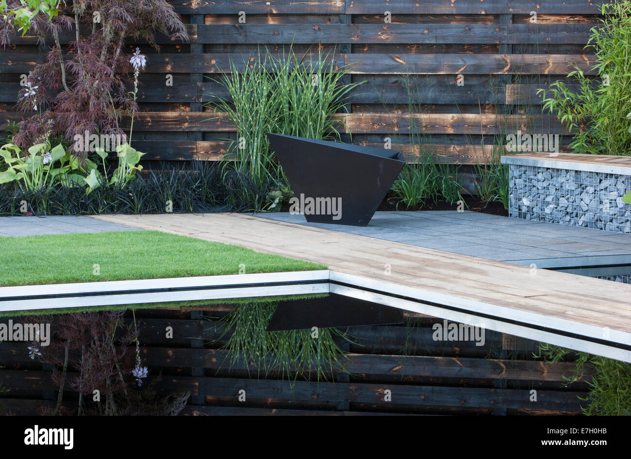 Giardino - Elemental - riflessivo scuro stagno di piscina con bruciato carbonizzato redwood bordo parete ciottoli di basalto in gabbia Foto Stock