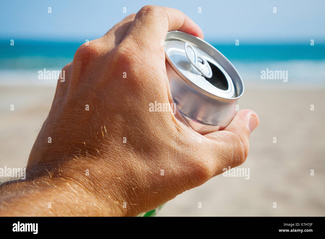 Bomboletta di alluminio di birra in una mano maschio con la spiaggia e il mare sullo sfondo Foto Stock