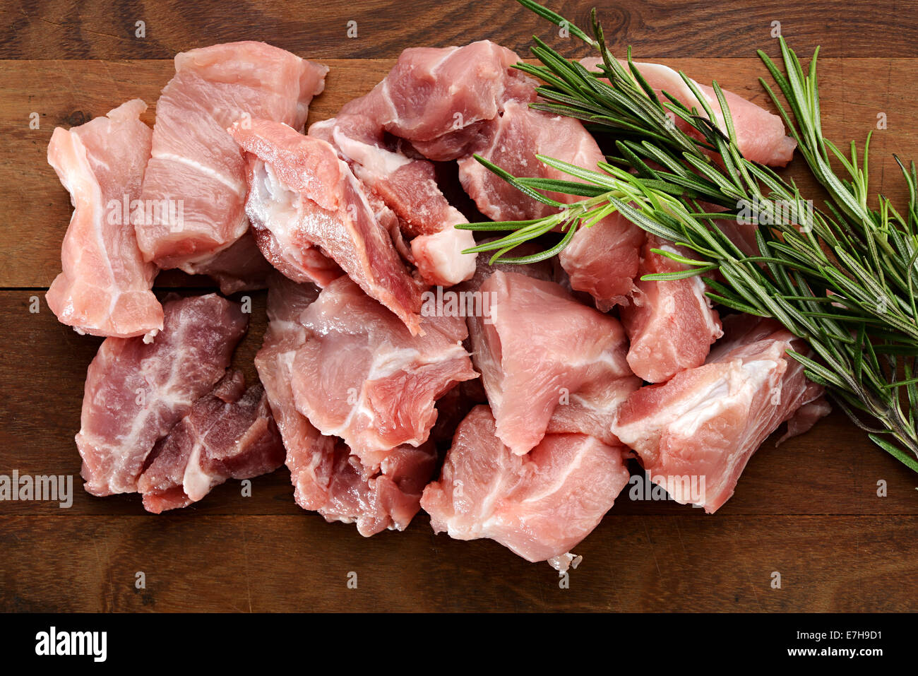 Tritate la carne cruda con un rametto di rosmarino fresco per il condimento e sapore su un tagliere di legno in attesa di essere cotti Foto Stock