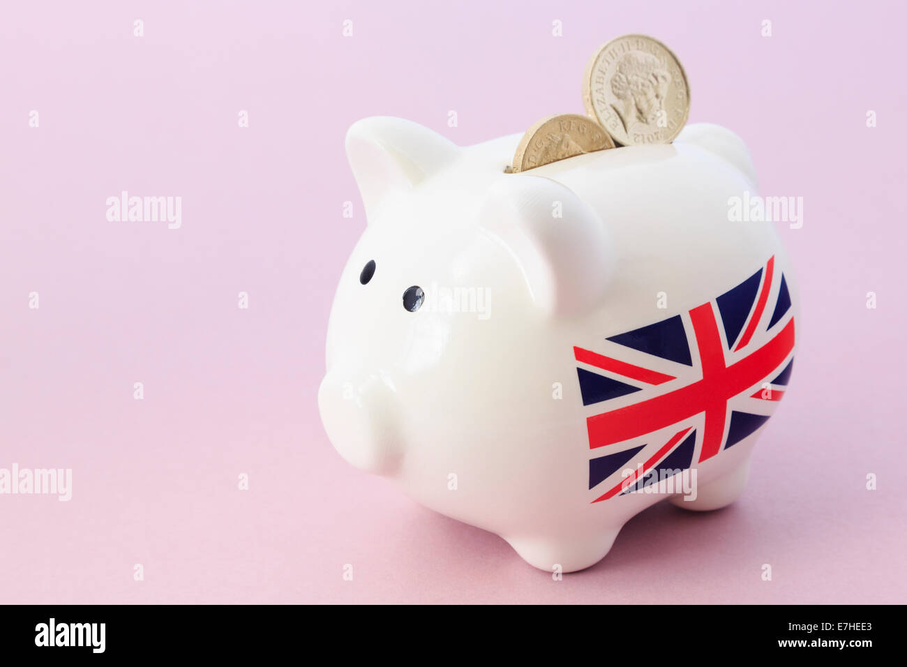 Salvadanaio con britannica Union Jack e due sterling pound monete nella slot su un sfondo di colore rosa. Regno Unito, Gran Bretagna Foto Stock