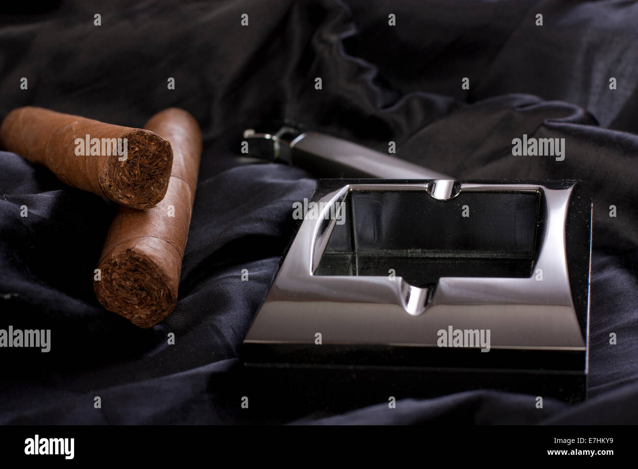 Chiudere metallico, posacenere e accendisigari sigaro cubano nero su sfondo di seta Foto Stock