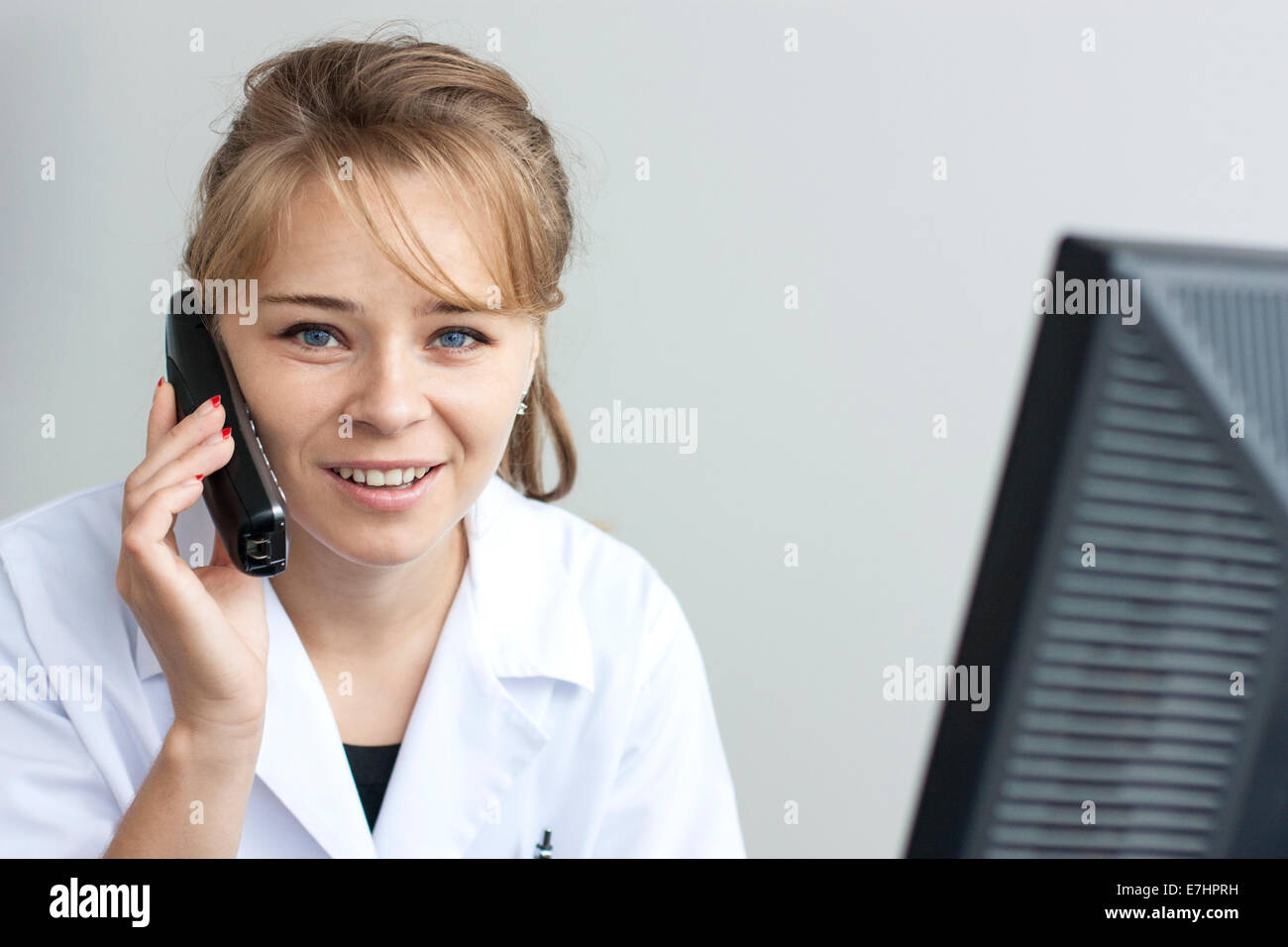 Immagine ravvicinata di bella donna farmacista tenendo il telefono e guardando con sorriso alla telecamera Foto Stock