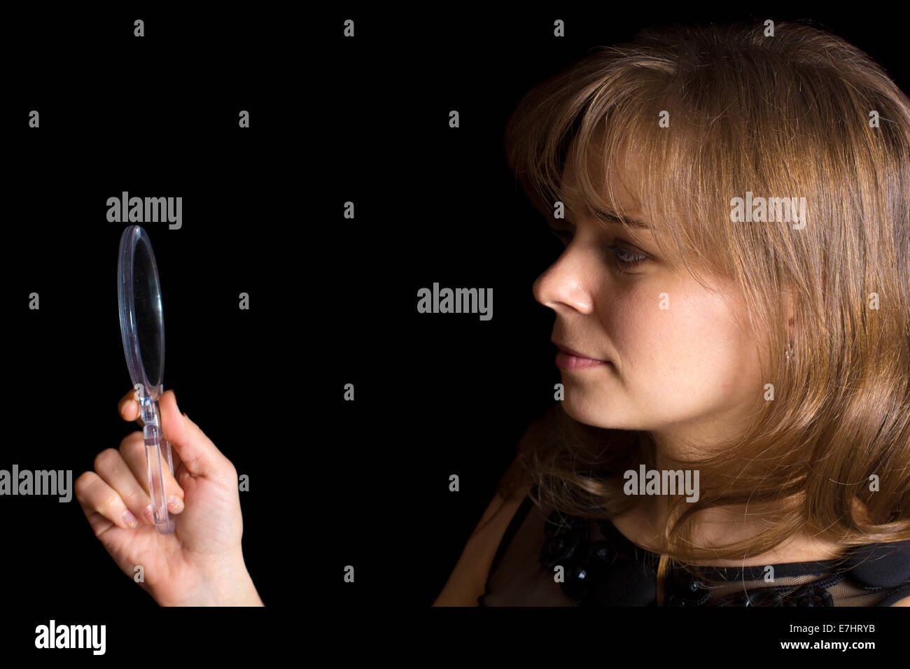 Una bambina guarda in uno specchio isolate su sfondo nero Foto Stock