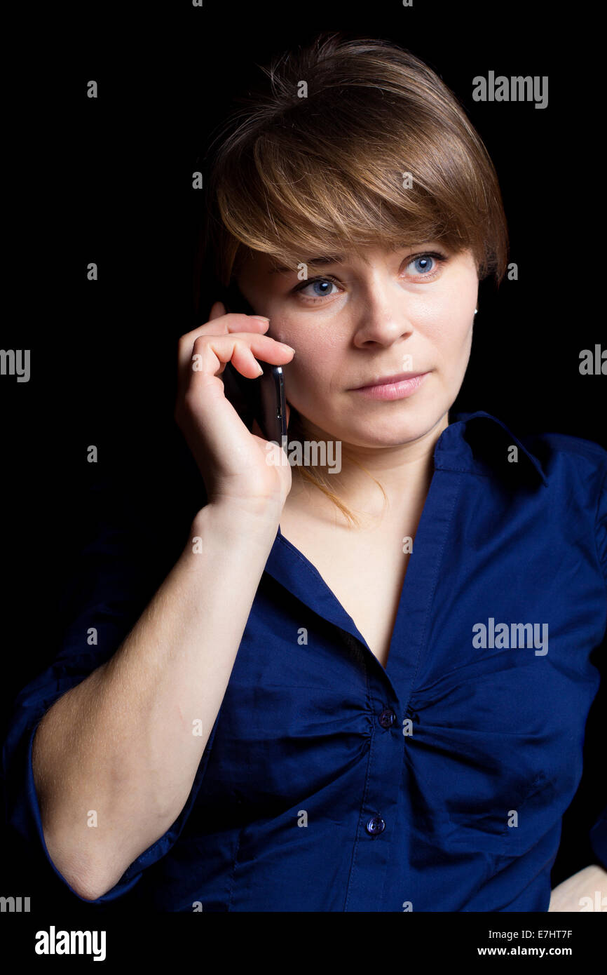 Giovane imprenditrice colloqui sul suo telefono cellulare, isolato su sfondo nero Foto Stock