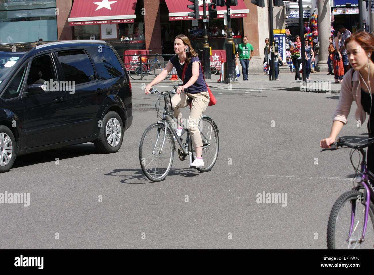 Due femmina i ciclisti in sella al fianco di un auto durante il loro viaggio intorno a una rotonda in Trafalgar Square, Londra Foto Stock