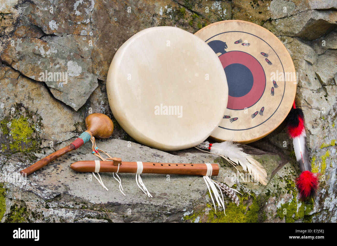 Due grandi, piatto, nativi americani tamburi con piume ornamentali e di un intaglio a mano di flauto traverso e shaker contro un muro di pietra naturale Foto Stock