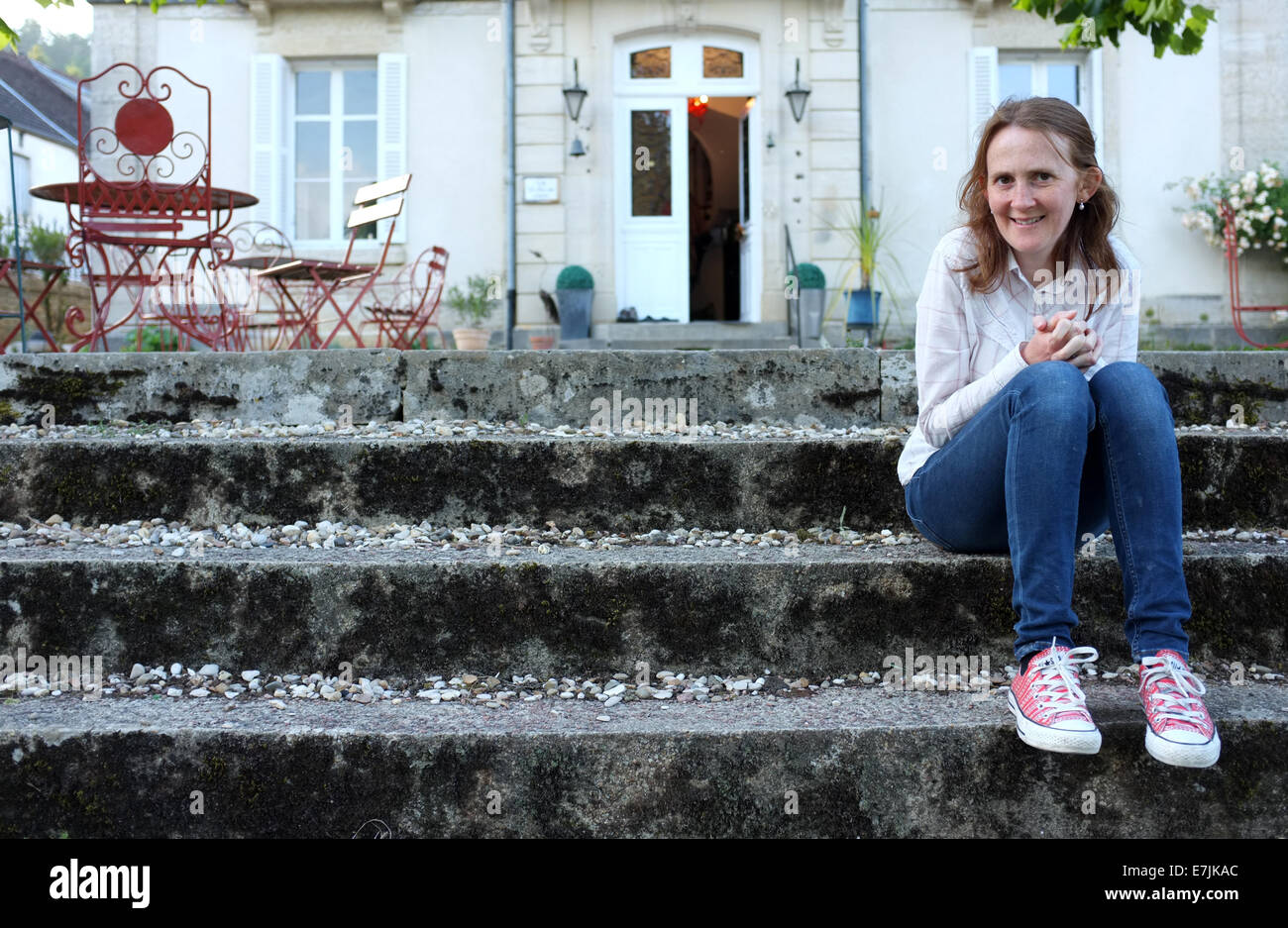 Dai capelli rossi donna seduta sui gradini di Chateau Francese sorridente. Abbigliamento Casual Foto Stock