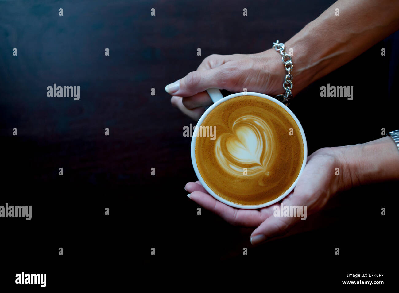 Coppia mani di una donna tenendo un caffè caffelatte cappuccino con un cuore design in schiuma Foto Stock
