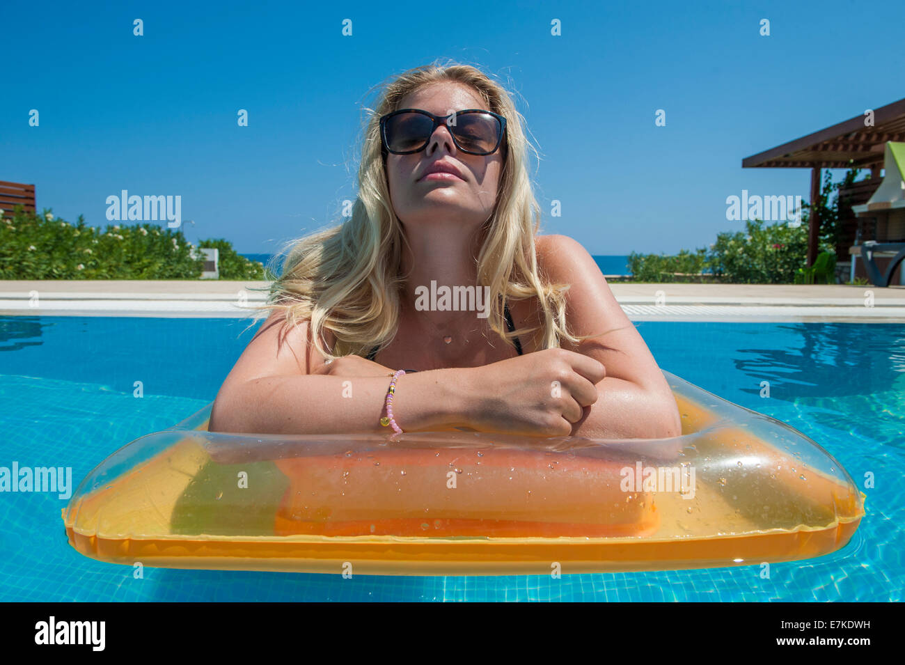 Una ragazza bionda in un bikini rosa e occhiali da sole giace su un letto gonfiabile in una piscina nel caldo sole Foto Stock